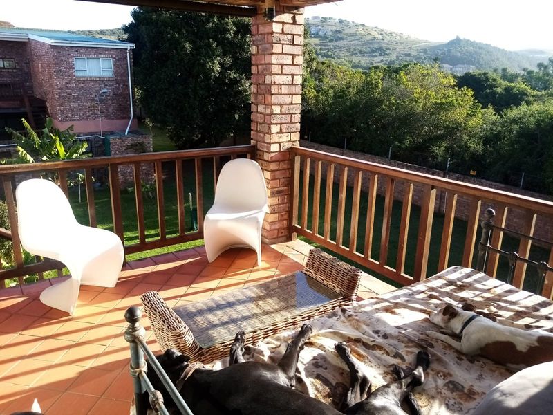 Covered balcony featuring terracotta tiling, a brick support pillar, and wooden balustrades, offering an elevated view of the surrounding garden and landscape.