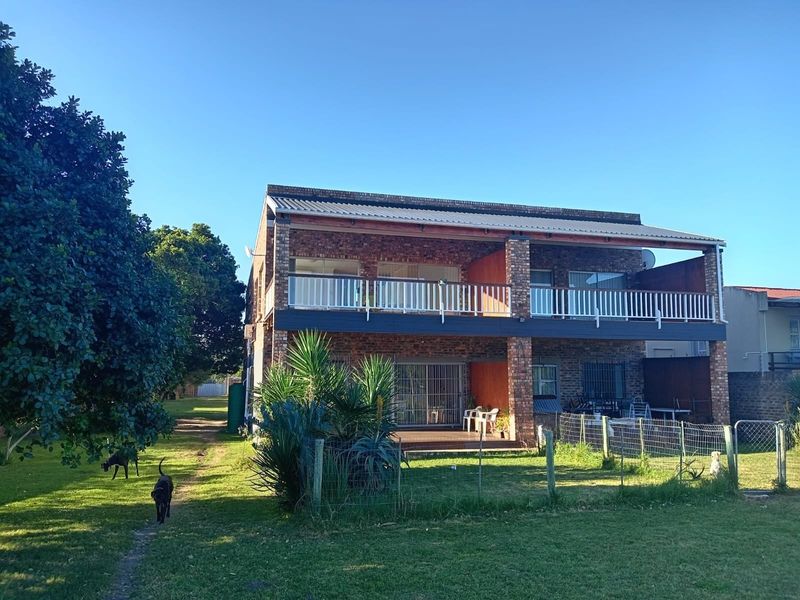 Rear view of a two-story brick house featuring an upper-level balcony, lower-level patio, and a spacious garden area.