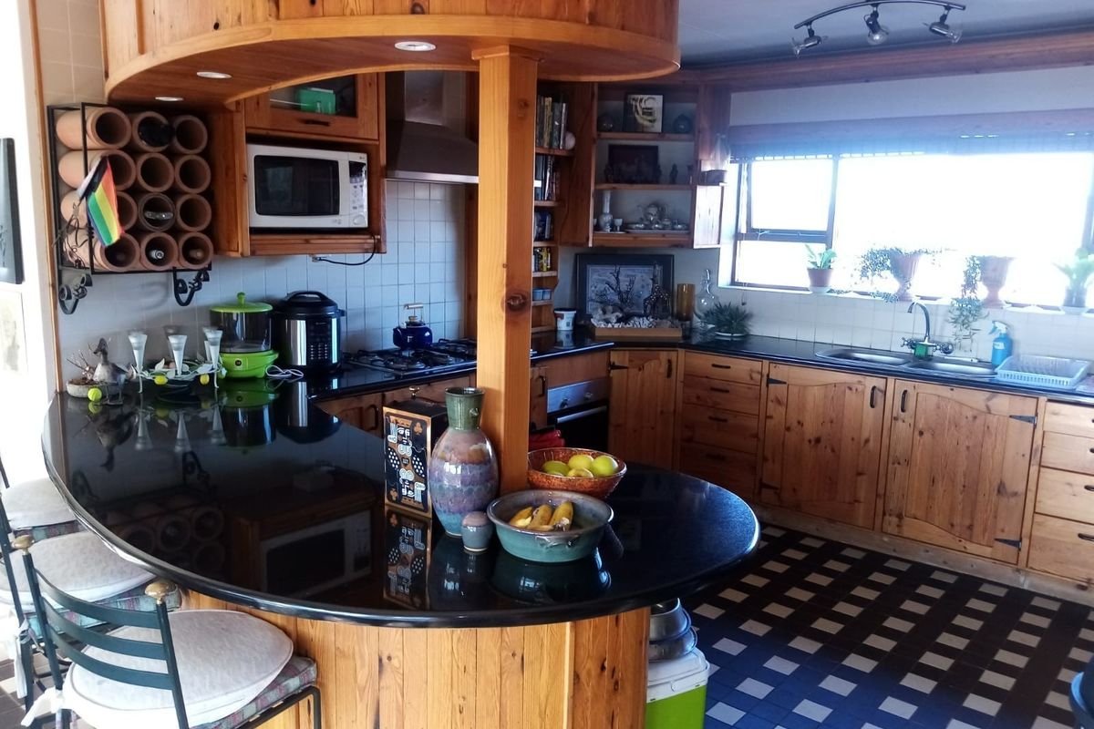 A functional kitchen featuring extensive wooden cabinetry, black granite countertops, a built-in breakfast bar, and integrated appliances with a classic, dated aesthetic.