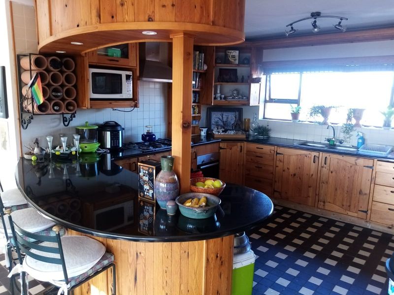 A functional kitchen featuring extensive wooden cabinetry, black granite countertops, a built-in breakfast bar, and integrated appliances with a classic, dated aesthetic.