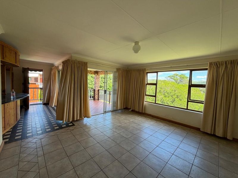 Spacious open-plan living area featuring tiled floors, a built-in breakfast bar, and large windows with access to an outdoor patio area.
