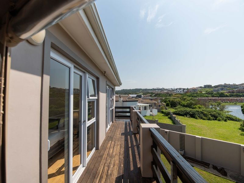 A spacious elevated balcony featuring timber decking and a railing, offering scenic views of the surrounding landscape and nearby water.
