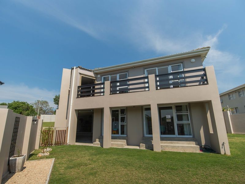 Rear view of a two-story house featuring a spacious upper balcony, ground-level patio access, and a well-maintained private garden area.