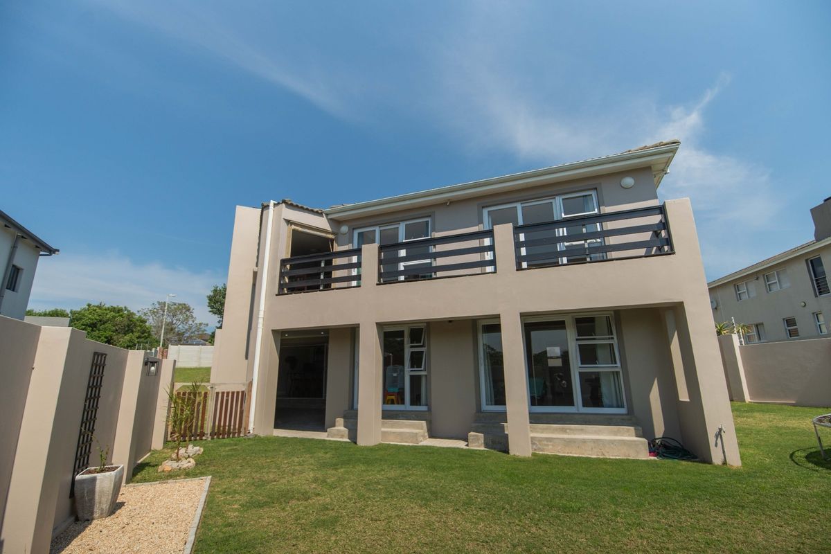 Rear view of a two-story house featuring a spacious upper balcony, ground-level patio access, and a well-maintained private garden area.