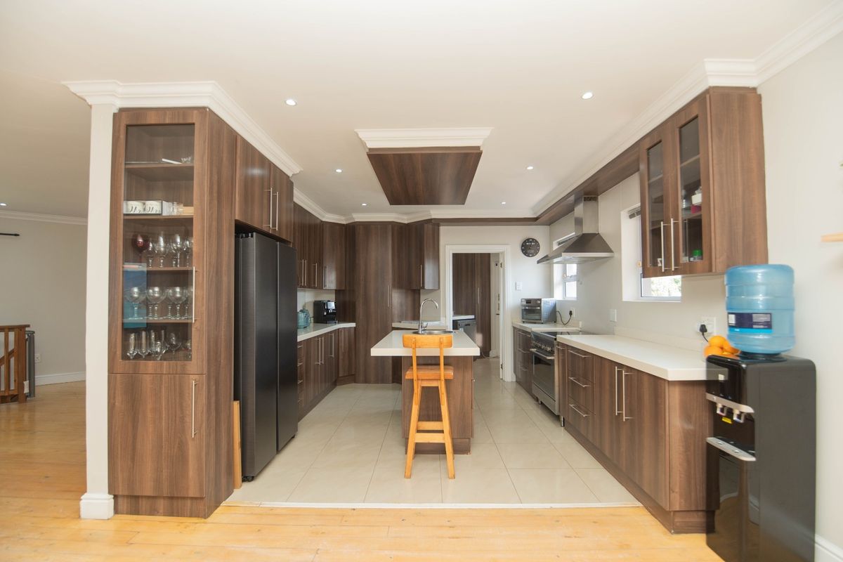 Modern kitchen featuring dark wood cabinetry, stone countertops, a central island, built-in oven, and stainless steel extractor fan with recessed lighting.
