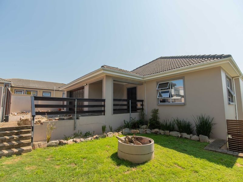 Rear view of the property featuring a landscaped garden, concrete fire pit, raised patio area with timber balustrade, and tiled roof.