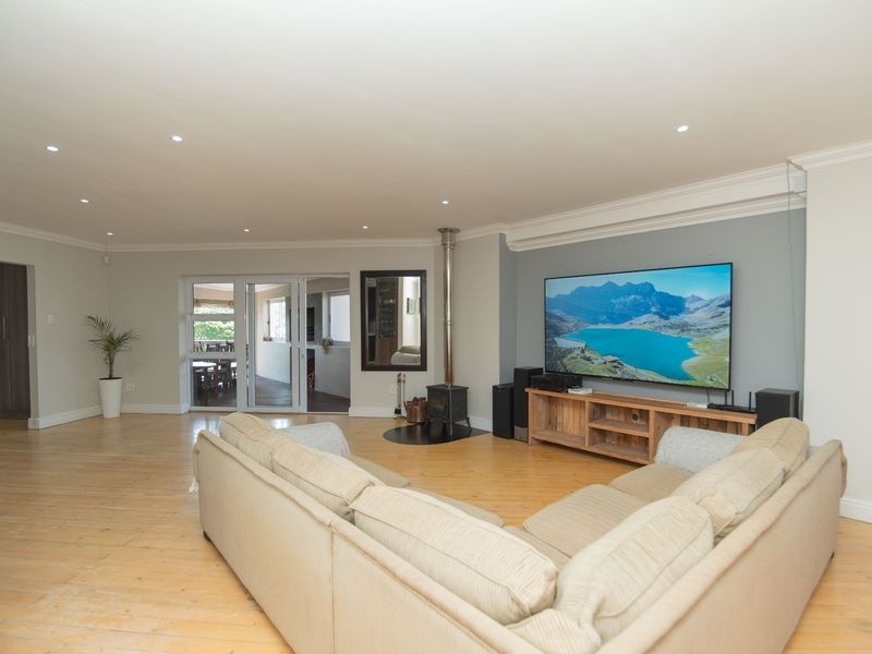 Spacious living room featuring light timber flooring, recessed downlights, crown molding, and a central wood-burning stove, with direct access to an outdoor patio area.