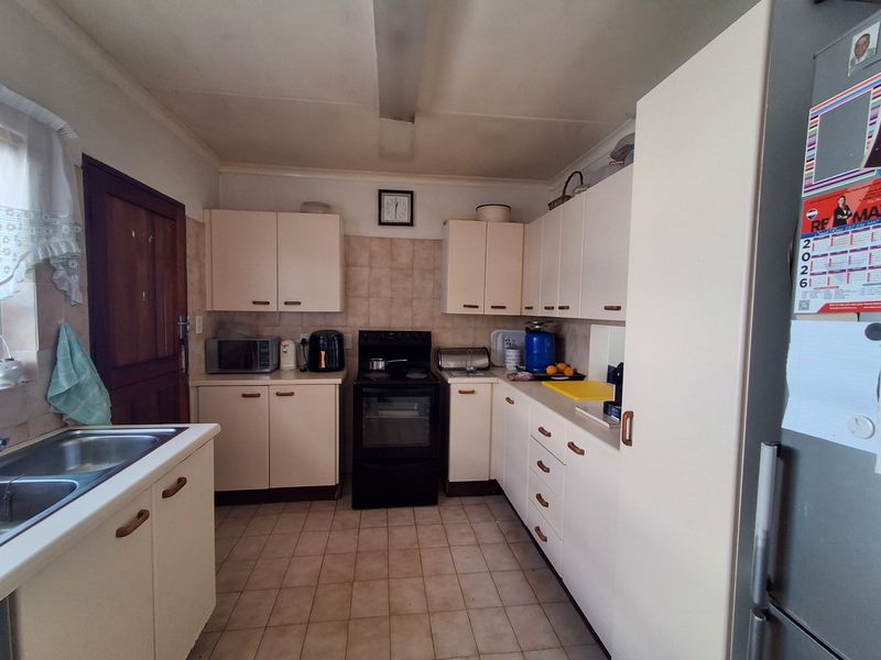 A functional kitchen featuring ample built-in cabinetry, a double stainless steel sink, tiled splashbacks, and a freestanding oven, offering a practical layout.