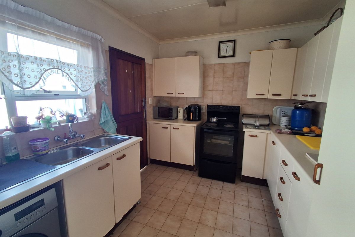 A functional kitchen featuring laminate cabinetry, a double bowl sink, tiled splashback, and a freestanding electric stove with ceramic floor tiles.