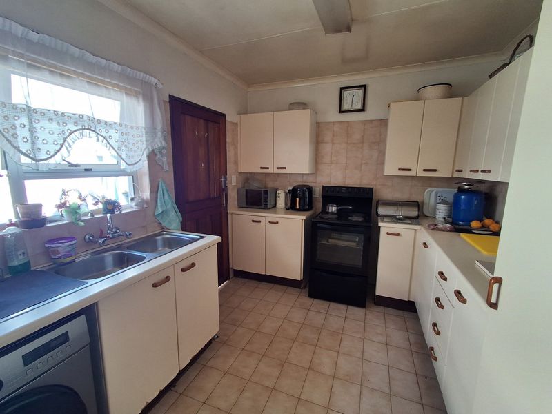 A functional kitchen featuring laminate cabinetry, a double bowl sink, tiled splashback, and a freestanding electric stove with ceramic floor tiles.