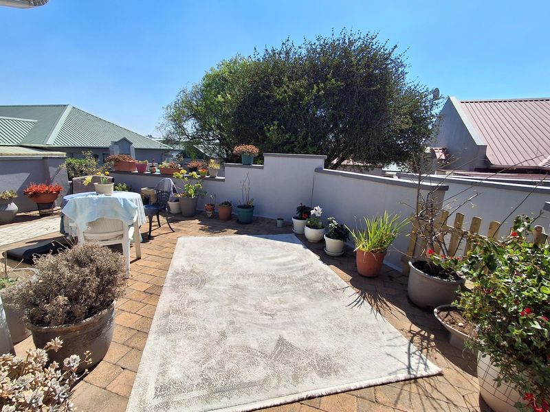 A sunny, open-air balcony featuring paved flooring and a low parapet wall, offering a pleasant outdoor space for relaxation.