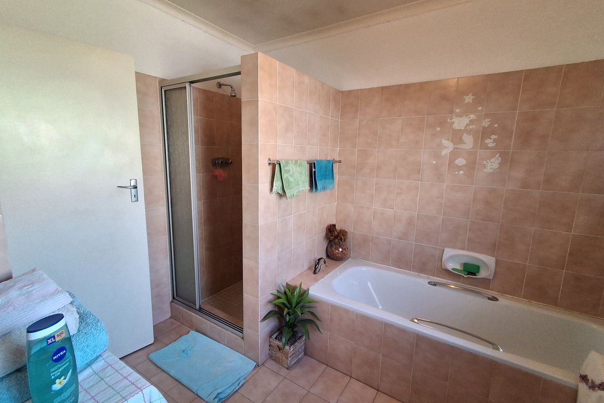 A functional bathroom featuring a built-in bathtub, separate shower enclosure, and neutral ceramic tiling throughout.