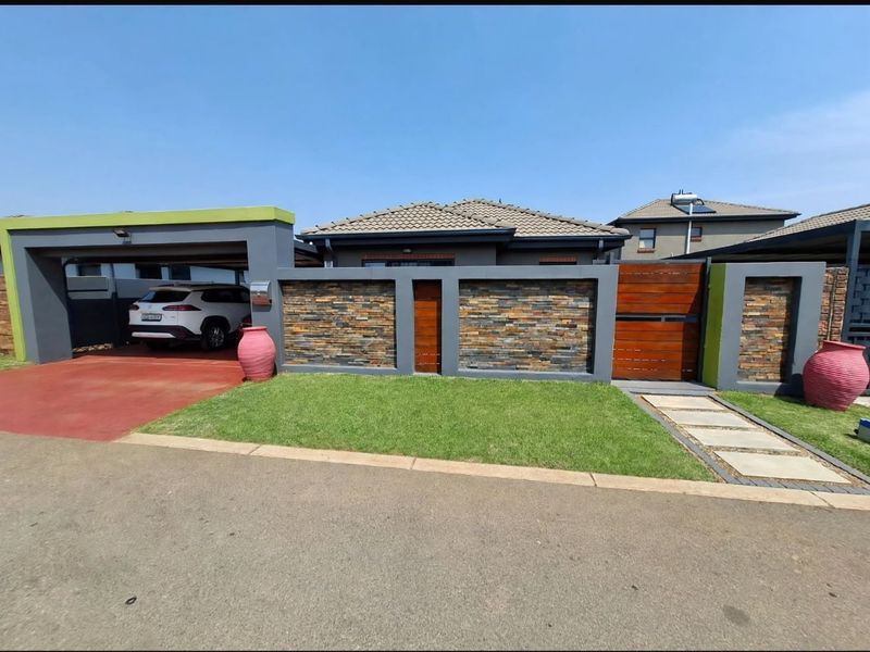Modern front facade featuring a stone-clad boundary wall, timber gate, paved walkway, and a covered carport area.