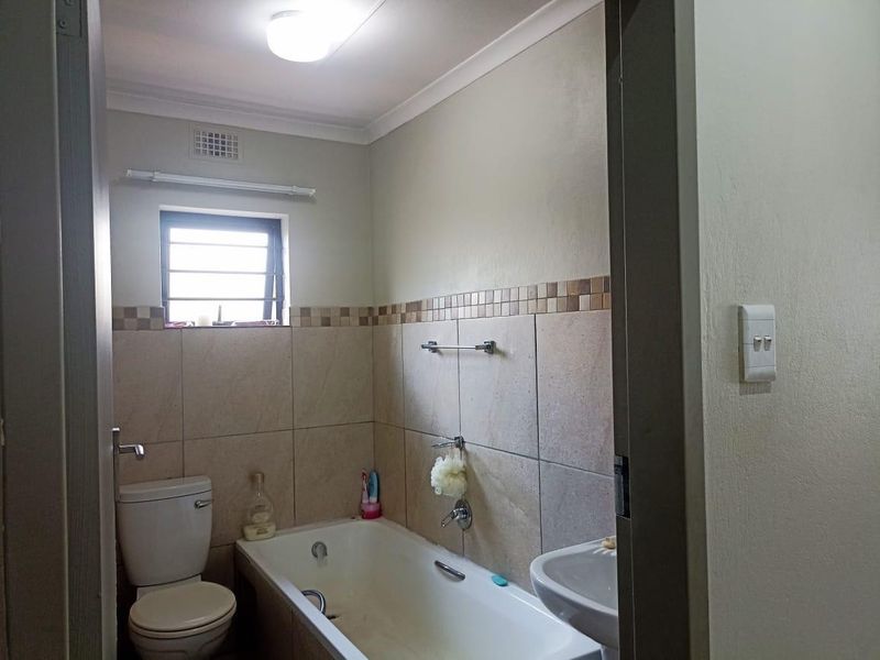A functional bathroom featuring a bathtub, pedestal basin, and toilet with neutral wall tiling and a window providing natural light.