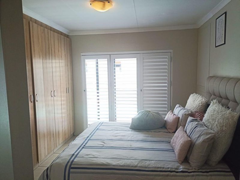 A well-maintained bedroom featuring built-in wooden cupboards and white shutter blinds, providing a clean and functional living space.