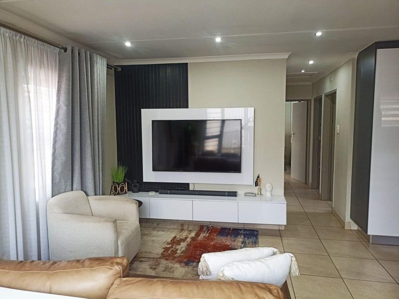 A modern living room featuring a sleek built-in media console, feature wall paneling, recessed downlights, and neutral tiled flooring.