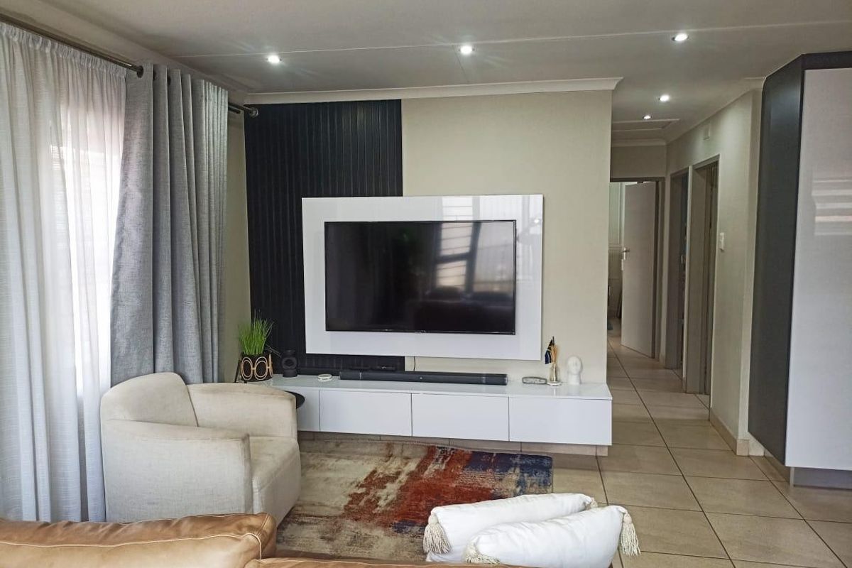 A modern living room featuring a sleek built-in media console, feature wall paneling, recessed downlights, and neutral tiled flooring.