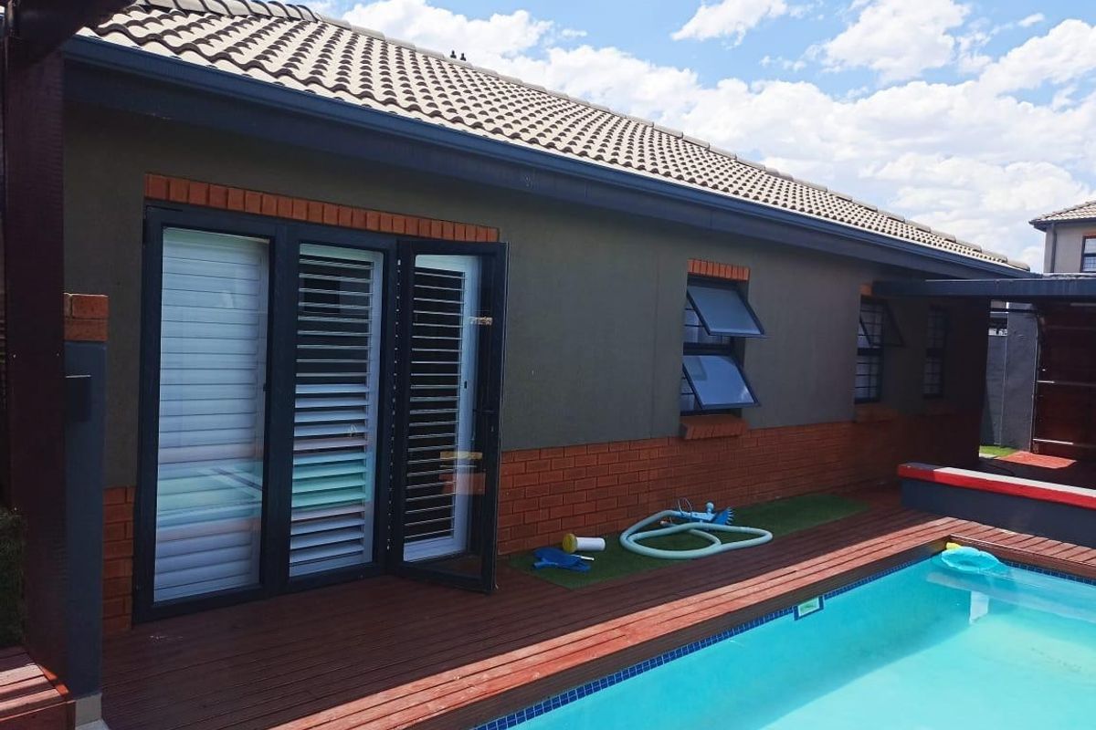 Rear exterior view featuring a swimming pool with timber decking, brick and rendered walls, and modern aluminium window and door frames.