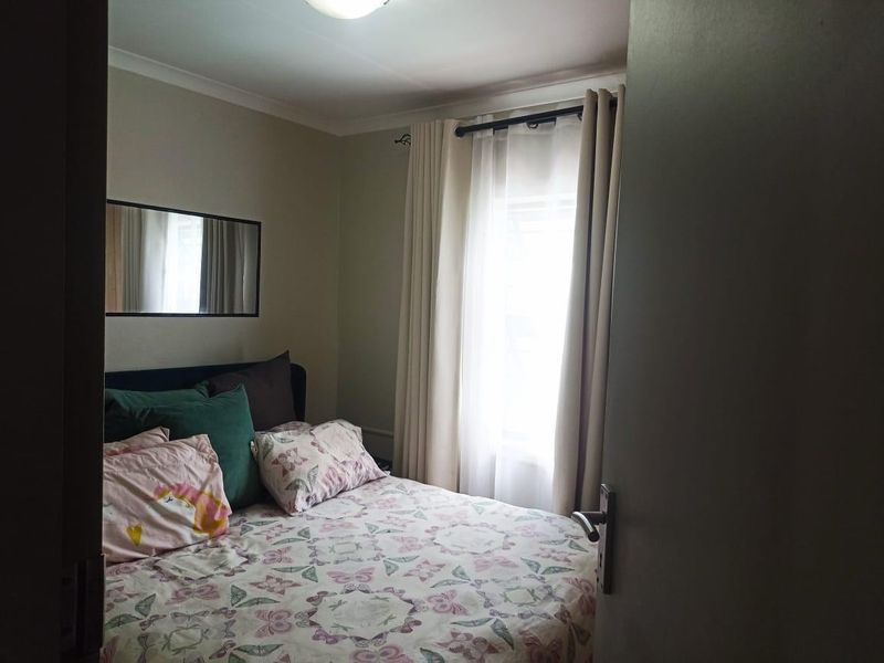 A cozy bedroom featuring neutral wall tones, a window with curtain treatments, and a ceiling light fixture.