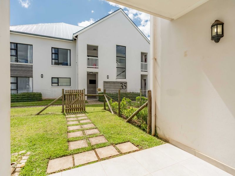 A view from a covered patio looking out onto a private garden area with a paved walkway and fenced perimeter in a modern apartment complex.