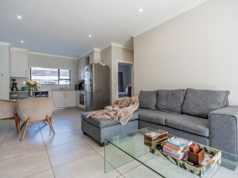 An open-plan living and kitchen area featuring modern tiled flooring, recessed lighting, and a functional kitchen layout with built-in cabinetry and appliances.