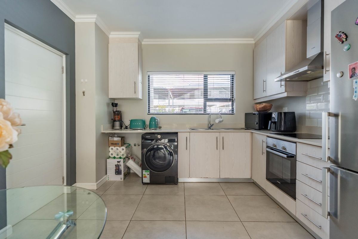 A functional kitchen featuring light wood-finish cabinetry, integrated oven, extractor fan, tiled flooring, and a window with venetian blinds.
