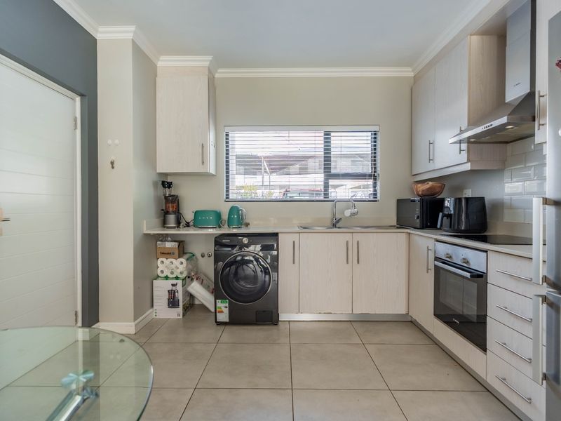 A functional kitchen featuring light wood-finish cabinetry, integrated oven, extractor fan, tiled flooring, and a window with venetian blinds.