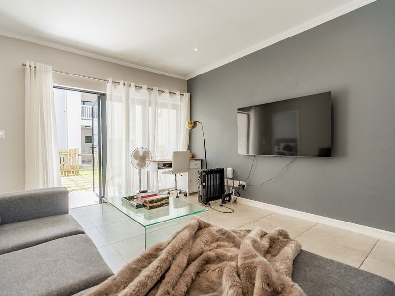 A bright living room featuring tiled flooring, a grey accent wall, and a sliding glass door providing direct access to the outdoor area.