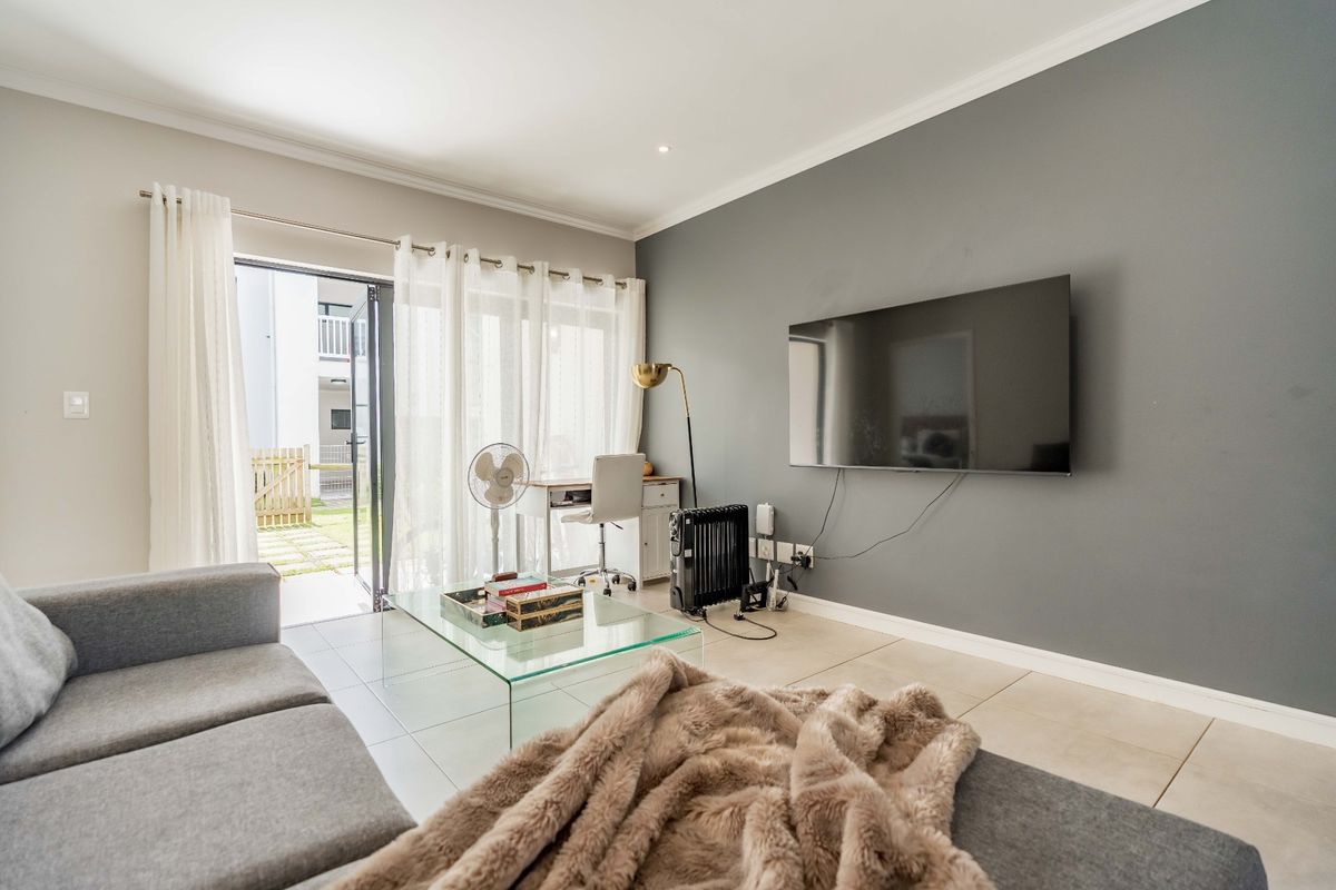 A bright living room featuring tiled flooring, a grey accent wall, and a sliding glass door providing direct access to the outdoor area.