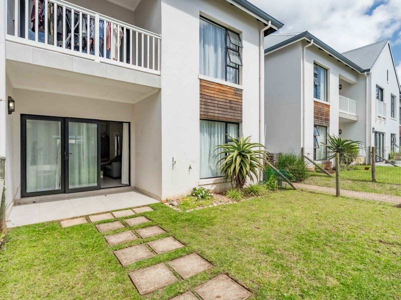 Rear view of a modern apartment building featuring a ground-floor tiled patio, sliding glass doors, and a private garden area with a stone pathway.