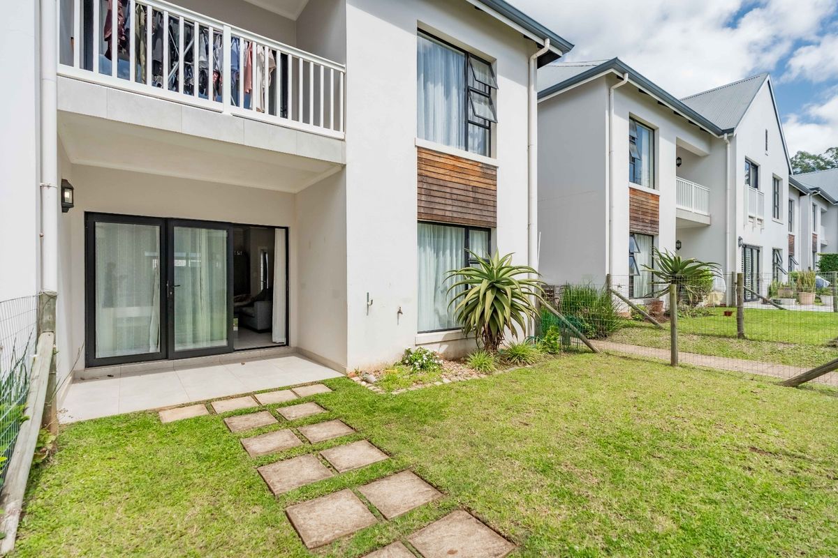 Rear view of a modern apartment building featuring a ground-floor tiled patio, sliding glass doors, and a private garden area with a stone pathway.