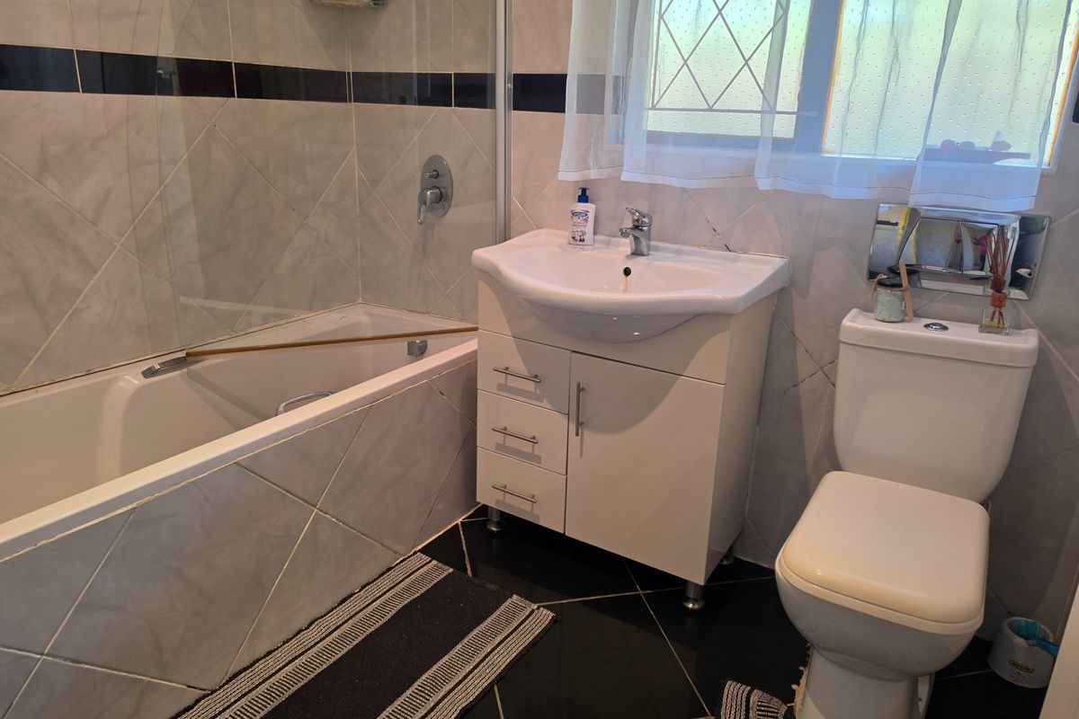 A functional bathroom featuring a bathtub with a glass screen, a modern vanity unit with a basin, and a standard toilet with tiled finishes.