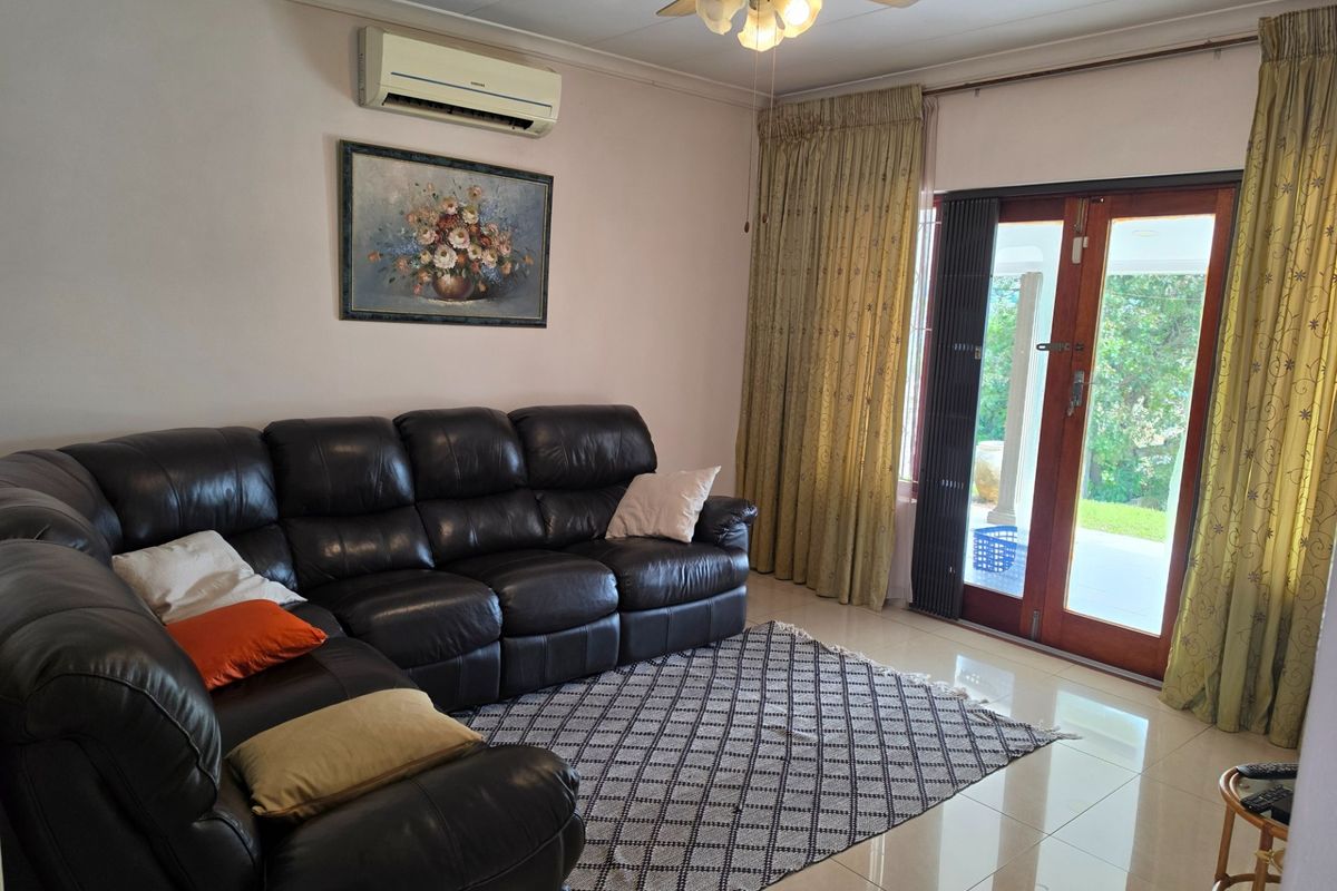 A comfortable living room featuring tiled flooring, a ceiling fan, a wall-mounted air conditioner, and double glass doors providing access to the outdoor area.