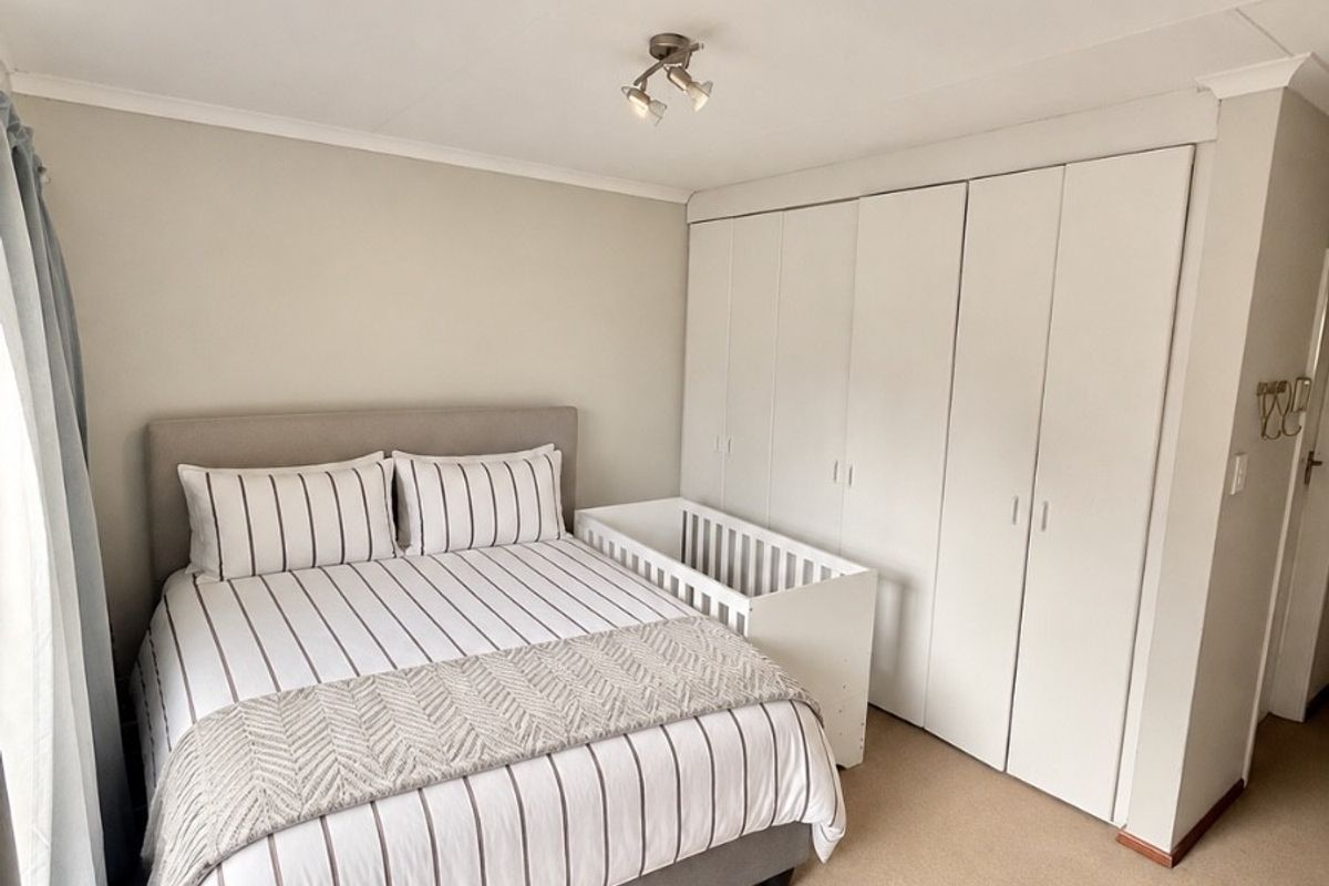 A well-maintained bedroom featuring neutral carpeting, built-in floor-to-ceiling cupboards, and a modern ceiling light fixture.
