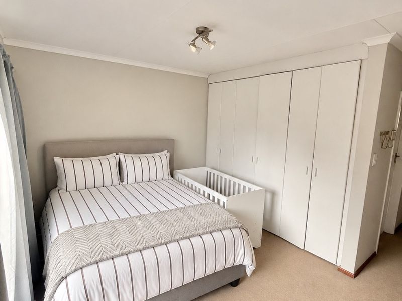 A well-maintained bedroom featuring neutral carpeting, built-in floor-to-ceiling cupboards, and a modern ceiling light fixture.