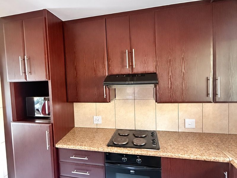 A functional kitchen featuring dark wood cabinetry, granite countertops, a built-in oven with electric hob, and a tiled backsplash.