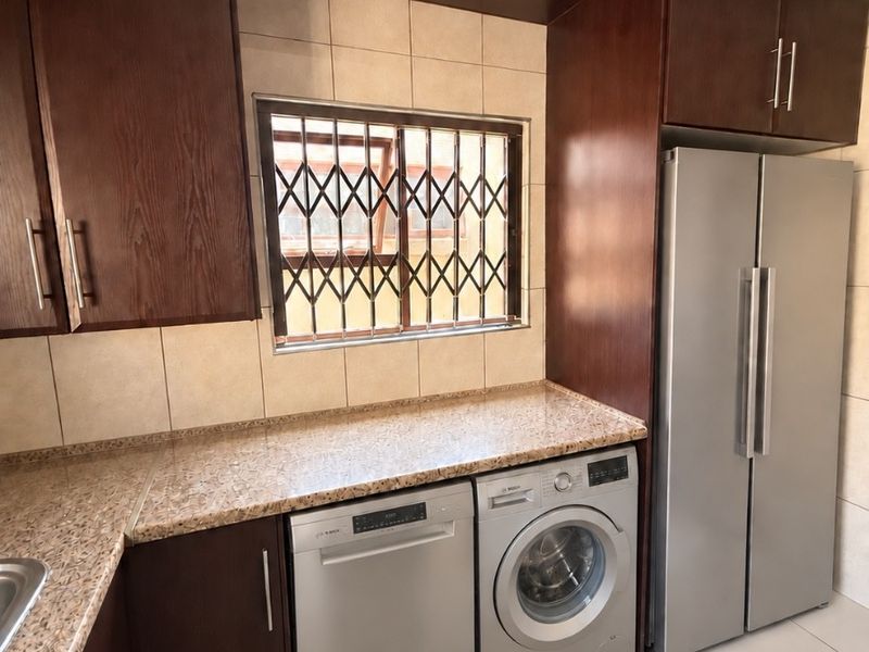 A functional kitchen featuring dark wood cabinetry, granite countertops, tiled backsplash, and integrated laundry and dishwasher appliances.