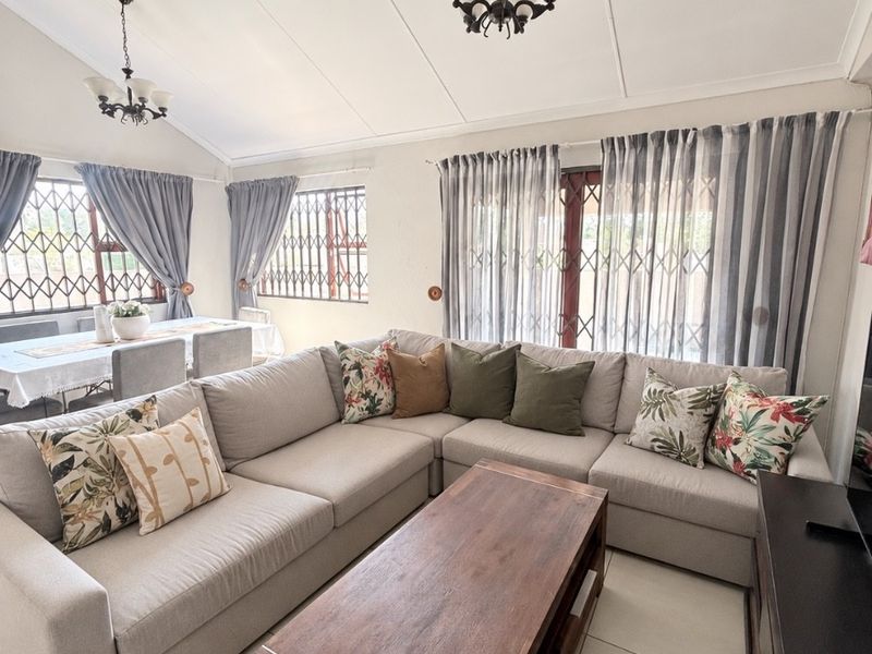 Spacious open-plan living and dining area featuring vaulted ceilings, tiled flooring, and large windows with security gates, providing a bright and airy atmosphere.