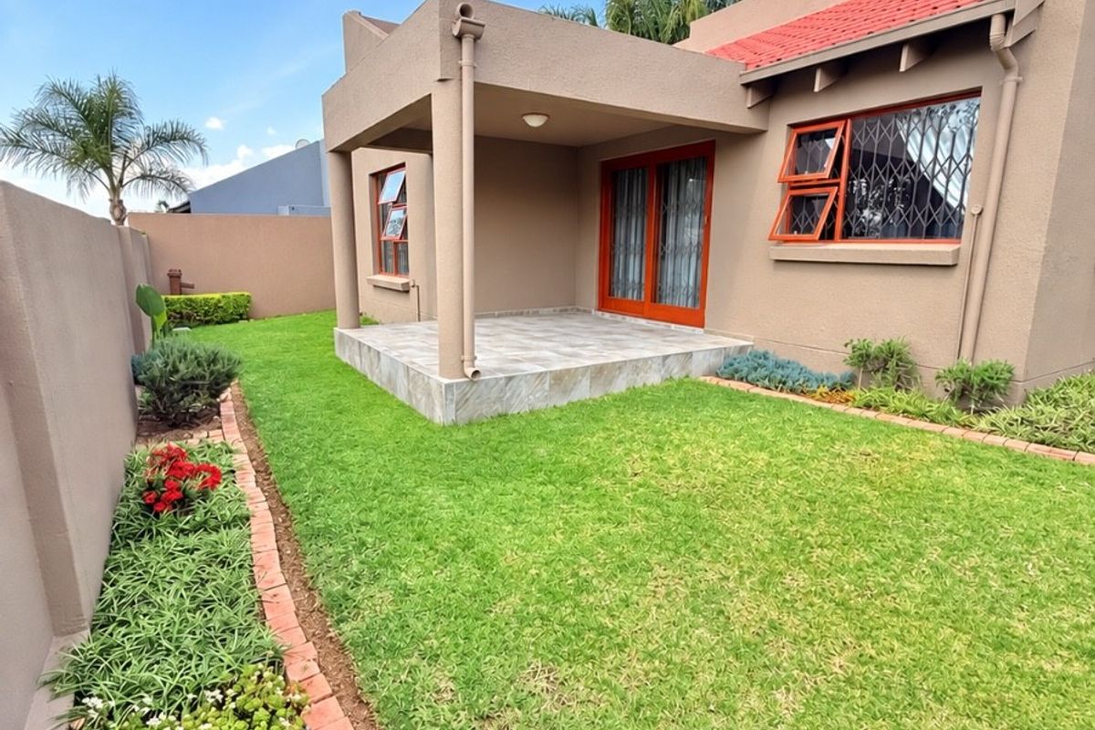A well-maintained rear exterior view featuring a covered patio, tiled flooring, and a neatly landscaped garden with brick-edged flower beds.