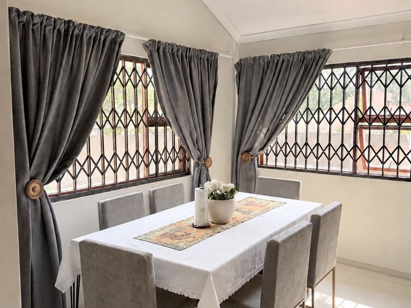 A bright dining room featuring a vaulted ceiling, tiled flooring, and large windows fitted with security gates.