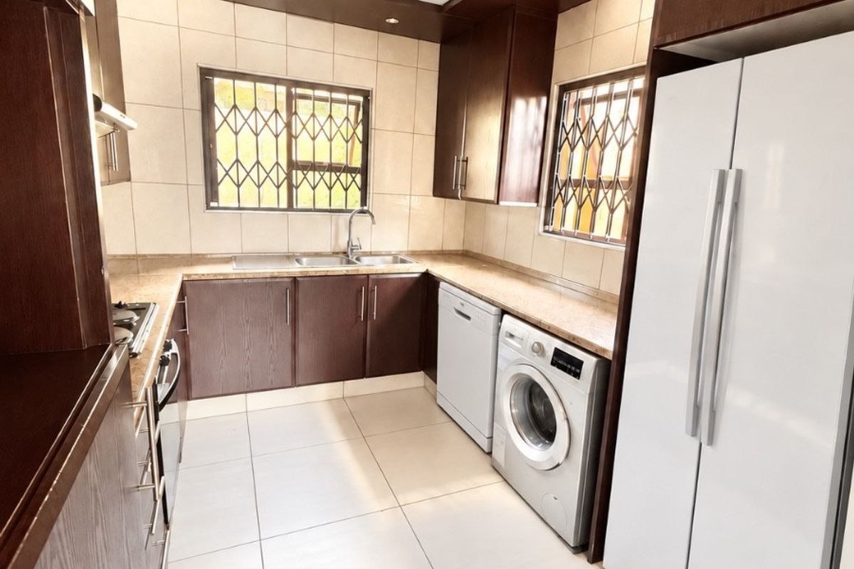A well-maintained kitchen featuring dark wood cabinetry, stone countertops, tiled flooring, and integrated appliances, offering a functional and clean workspace.