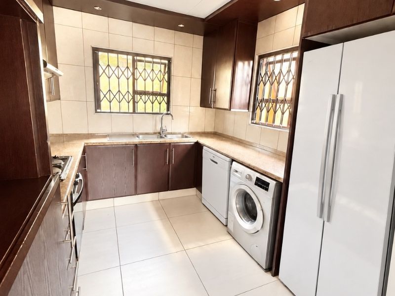 A well-maintained kitchen featuring dark wood cabinetry, stone countertops, tiled flooring, and integrated appliances, offering a functional and clean workspace.