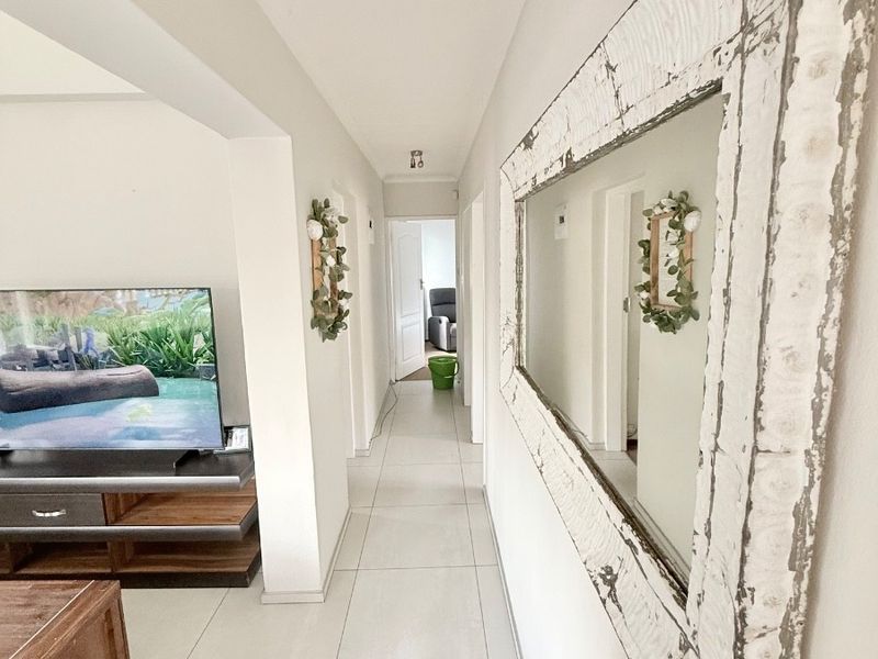A bright, tiled hallway connecting the living area to the rest of the home, featuring neutral finishes and a clean layout.