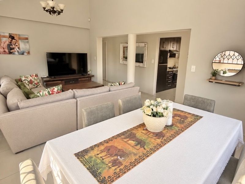 Spacious open-plan living and dining area featuring vaulted ceilings, elegant chandeliers, and neutral tiled flooring, with a seamless flow into the kitchen space.