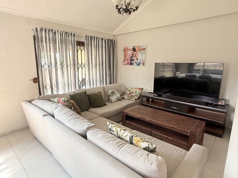 A comfortable living room featuring a vaulted ceiling, neutral ceramic floor tiles, and a security gate over the window.