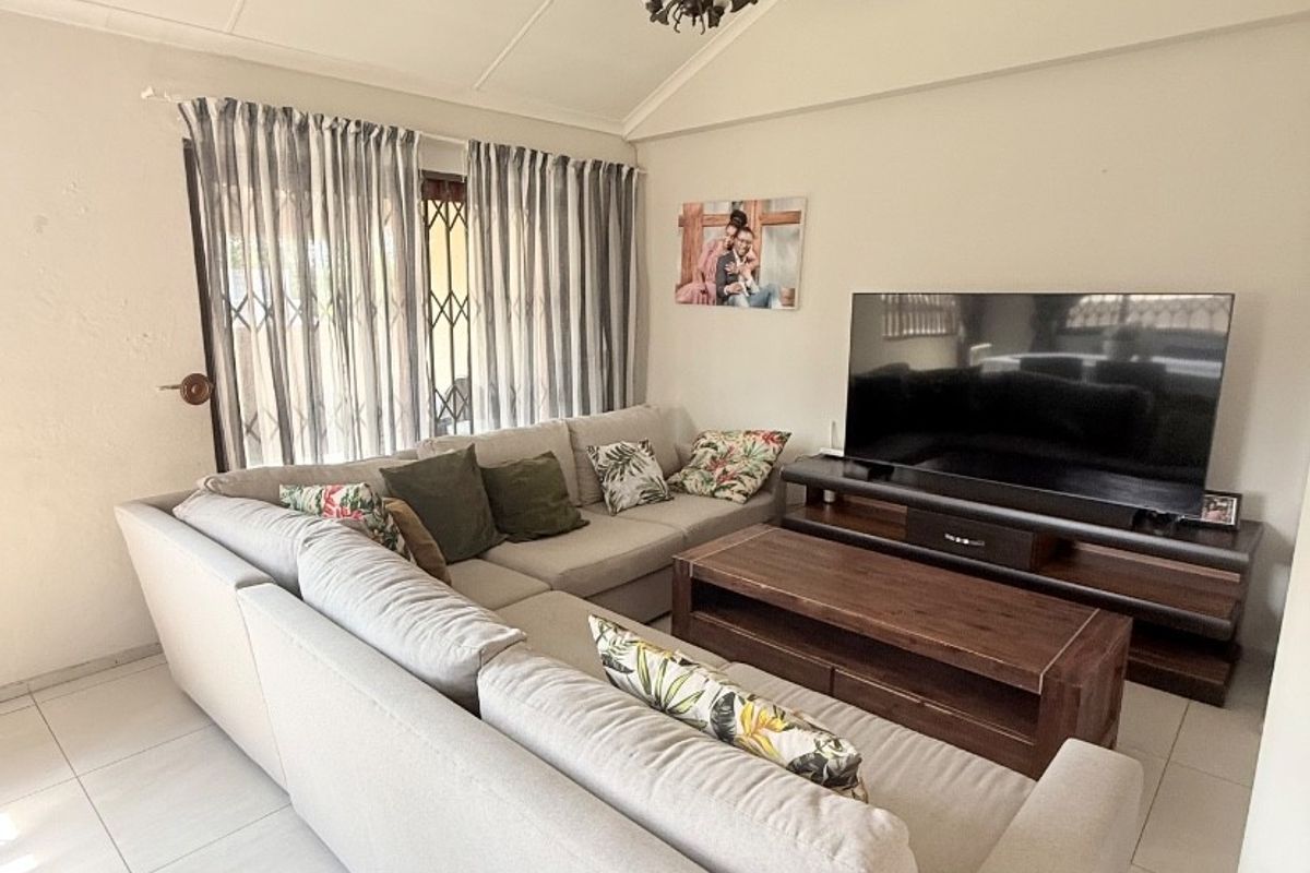 A comfortable living room featuring a vaulted ceiling, neutral ceramic floor tiles, and a security gate over the window.