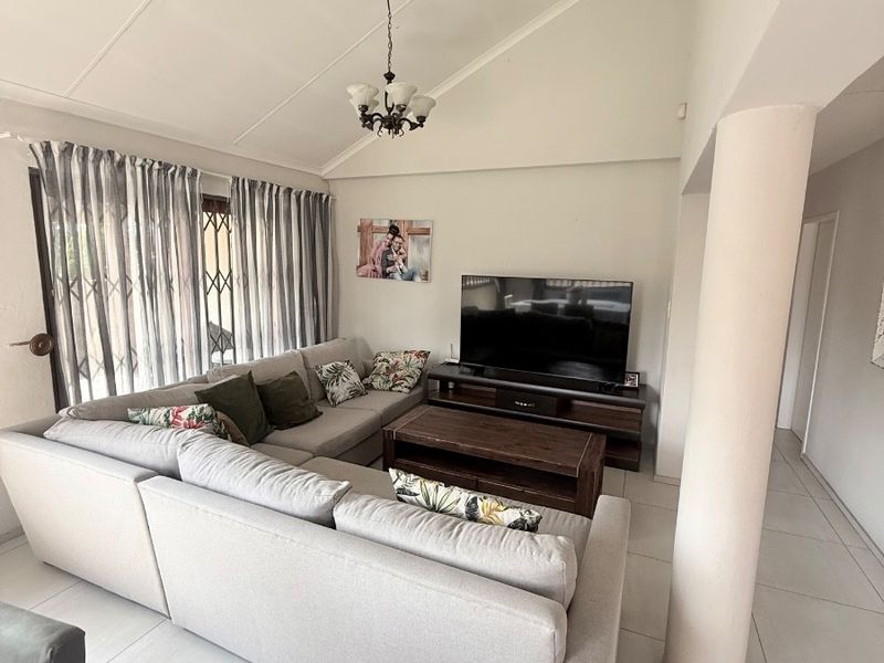 A bright living room featuring a vaulted ceiling, tiled flooring, and a structural column, providing an open and airy atmosphere.