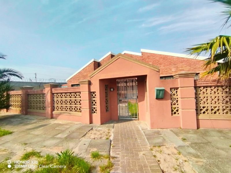 Front entrance view featuring a brick boundary wall with decorative breeze blocks, a metal security gate, and a paved walkway leading to the property.