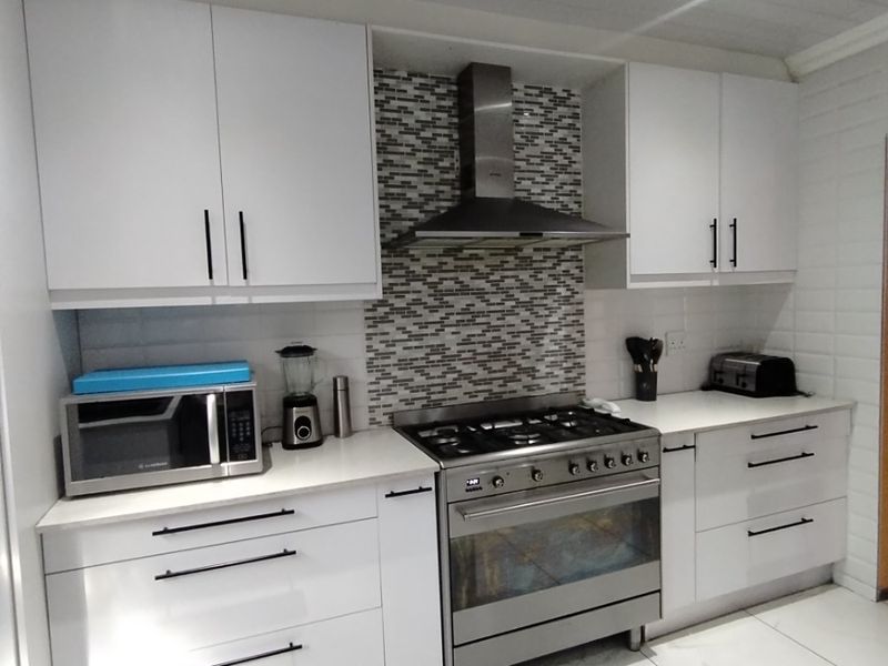 Modern kitchen featuring white cabinetry, stone countertops, a stainless steel gas stove with extractor fan, and a decorative mosaic tile backsplash.