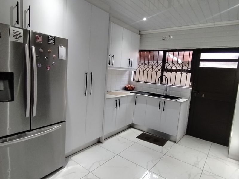 Modern kitchen featuring white cabinetry, marble-look floor tiles, a double sink, and a secure exterior door with security gate.